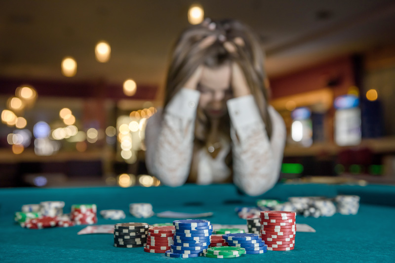 Gambling Addiction -Upset woman in casino sitting behind poker table