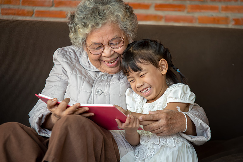 Happy Asian grandmother reading a book to her granddaughter