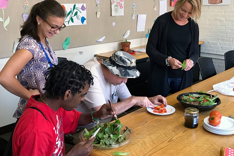 Stephanie Natelli, MS, LMHC (standing left) and Kathy Hagendorf (standing right) help program participants prepare a healthy salad with vegetables that the group grew and harvested