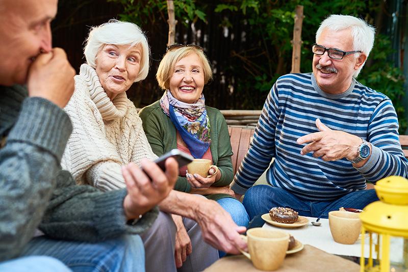 Group of cheerful seniors enjoying time together drinking tea outdoors in cafe and sharing life stories in retirement