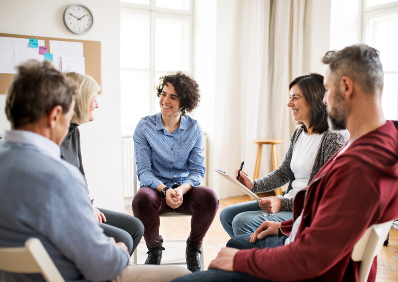 Men and women sitting in a circle during group therapy, talking.