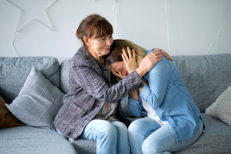 Older mother hugging crying adult daughter who is depressed to show support and care