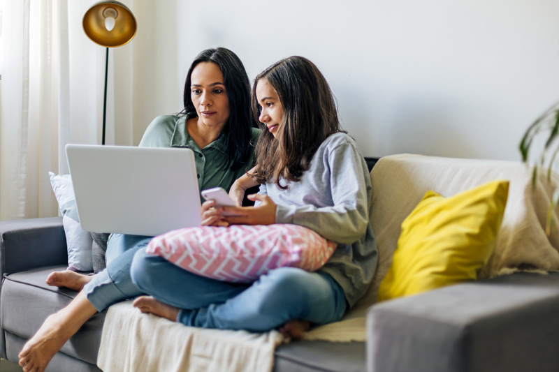 mother sitting with daughter on a couch taking an online assessment on a laptop