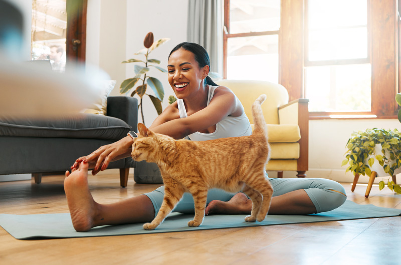 Happy woman stretching legs petting her cat in her home