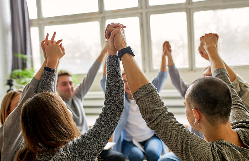 Young adults celebrating recovery from alcohol addiction at an AA meeting with their hands raised up together