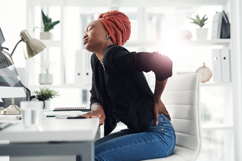 woman sitting at a desk and holding her back in pain