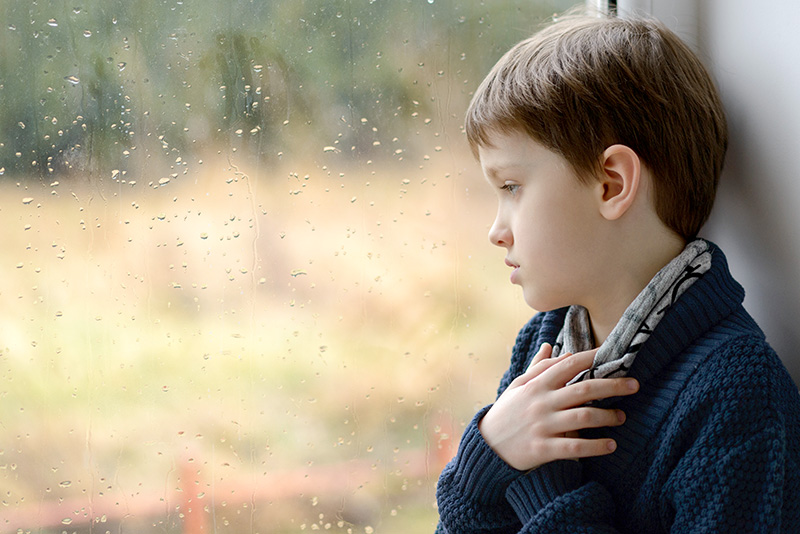 A sad boy looking through a window on a rainy day