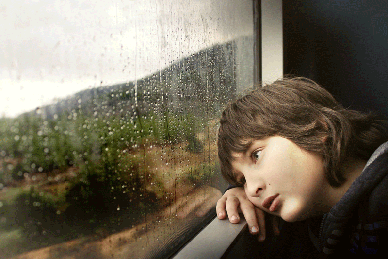 depressed teenage boy looks out window