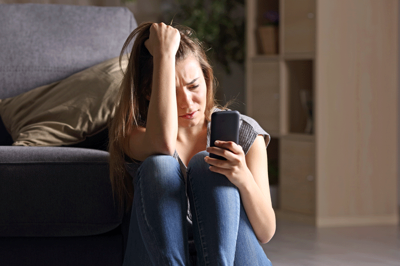 Sad teen checking social media on her phone at home