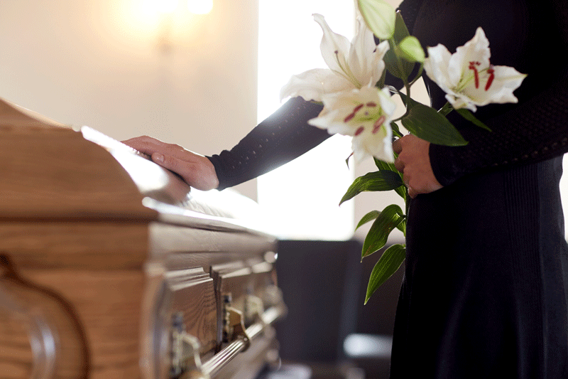 Grieving woman with white lily flowers and coffin at a funeral