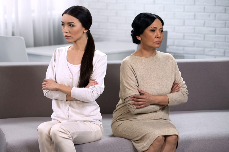 South Asian mother-in-law and daughter-in-law sitting crossed arm on the couch