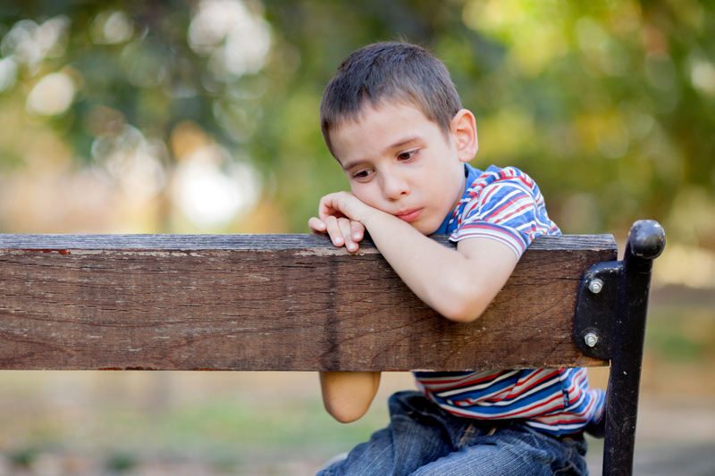 unhappy boy sitting on a park bench and crying
