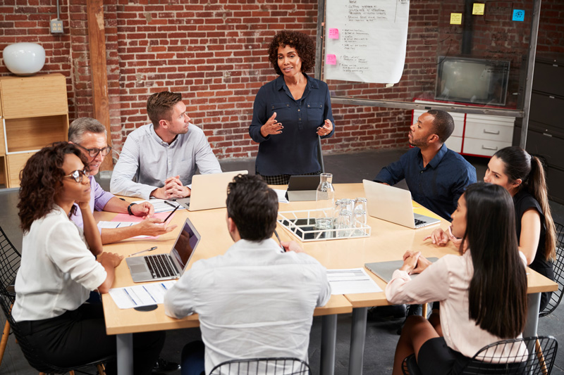 Mature Businesswoman Standing And Leading Office Meeting Around Table