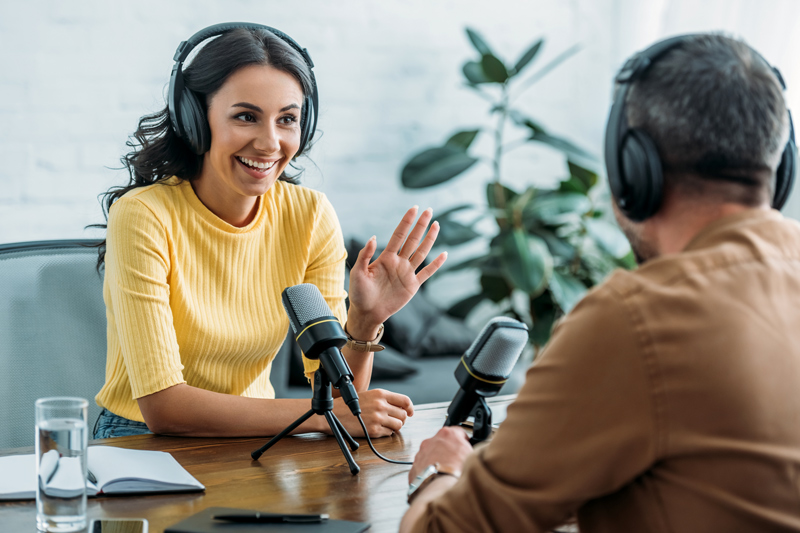 smiling radio host gesturing while talking to colleague in broadcasting studio